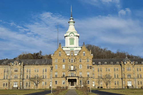 Historic building with a tall clock tower, surrounded by trees and a clear blue sky.