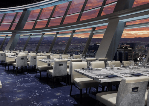 Elegant restaurant interior with large windows showcasing a sunset view over a city skyline.