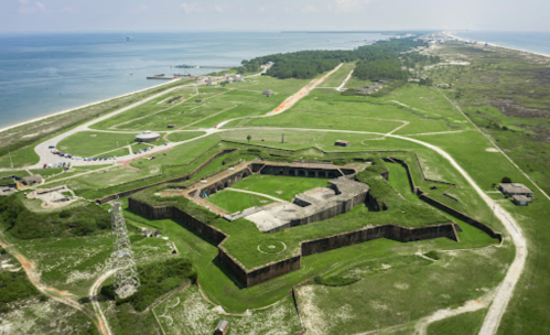 Aerial view of a historic star-shaped fort surrounded by green landscape and water in the background.