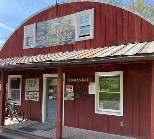 A rustic red building with a metal roof, featuring a sign for Linney's Mill Store and a bike parked outside.