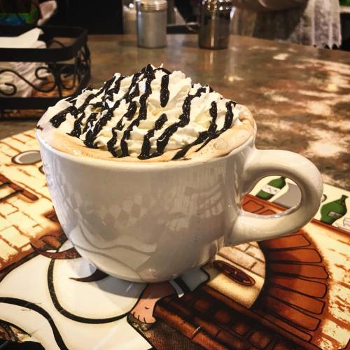 A large white mug filled with hot chocolate topped with whipped cream and drizzled chocolate sauce.