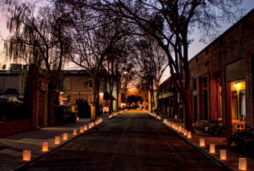 A quiet street lined with glowing lanterns, trees silhouetted against a twilight sky.