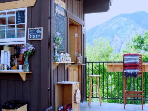 A cozy outdoor café with a chalkboard menu, flowers, and mountain views in the background.