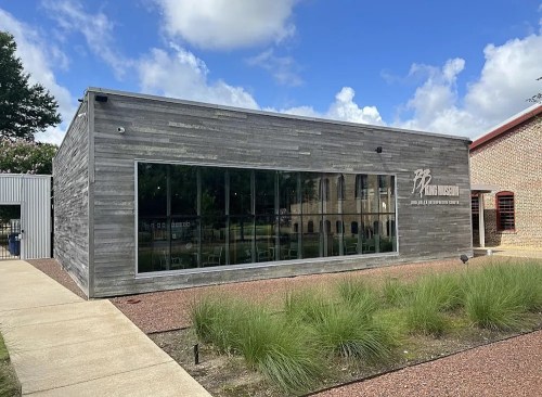 Modern building with large windows, wooden exterior, and a sign reading "The Mill" against a blue sky with clouds.
