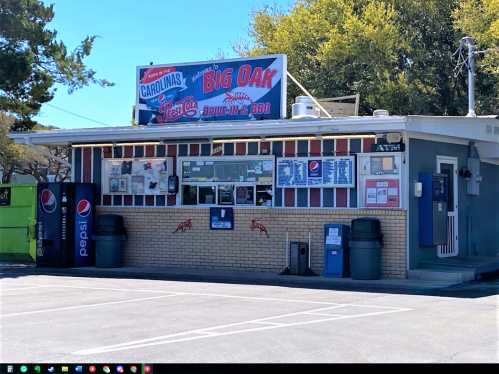 A drive-in restaurant with a sign reading "Big Oak" and a menu displayed on the wall, surrounded by trees.