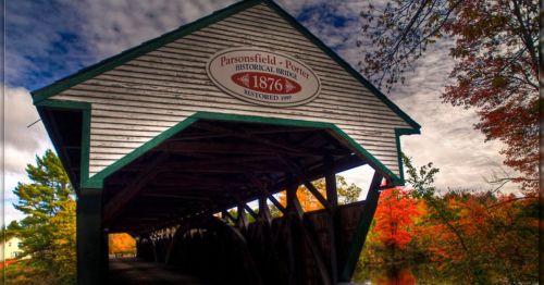 Historic covered bridge with a sign reading "Parsonsfield-Porter, 1876, restored 1991," surrounded by autumn foliage.