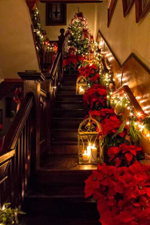 A beautifully decorated staircase with Christmas lights, poinsettias, and lanterns, creating a festive atmosphere.