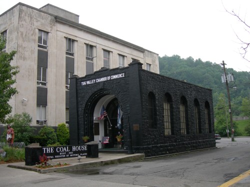 A stone building with arched windows, labeled "The Coal House," next to a larger gray structure, surrounded by greenery.