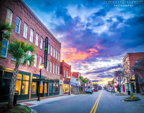 A colorful sunset over a charming downtown street lined with historic buildings and palm trees.
