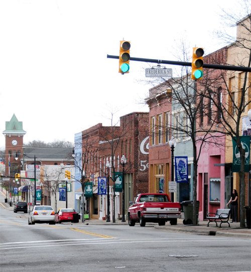 A quiet downtown street with colorful storefronts, traffic lights, and a clock tower in the background.