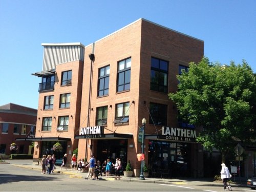 A brick building with large windows, featuring "ANTHEM Coffee & Tea" signage, on a sunny day with pedestrians nearby.