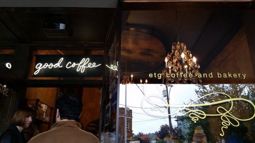 A cozy coffee shop entrance with a neon sign reading "good coffee" and a chandelier visible inside.