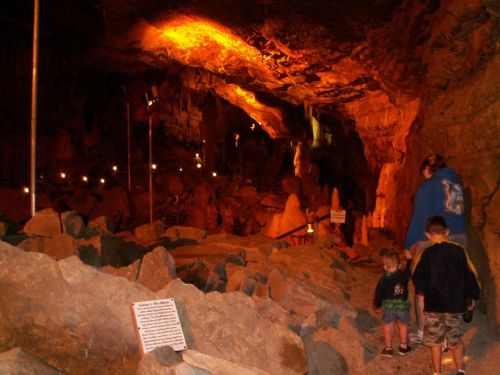 A family explores a dimly lit cave with rocky terrain and warm orange lighting.