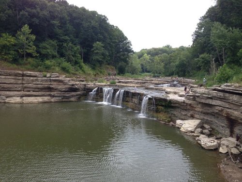 A serene landscape featuring a waterfall cascading into a calm pool, surrounded by rocky cliffs and lush greenery.