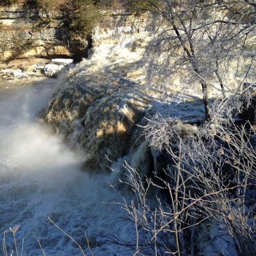 A waterfall cascading over rocky cliffs, surrounded by frosty trees and mist rising from the water.
