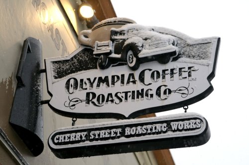 Sign for Olympia Coffee Roasting Co. featuring a vintage truck and snow, with "Cherry Street Roasting Works" below.