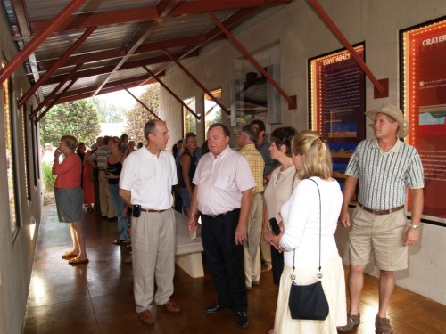 A group of people converses and observes displays in a well-lit indoor space with informational posters on the walls.