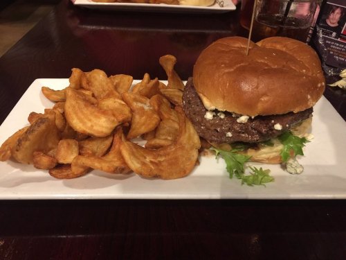 A plate featuring a burger with blue cheese and lettuce, accompanied by crispy potato chips.