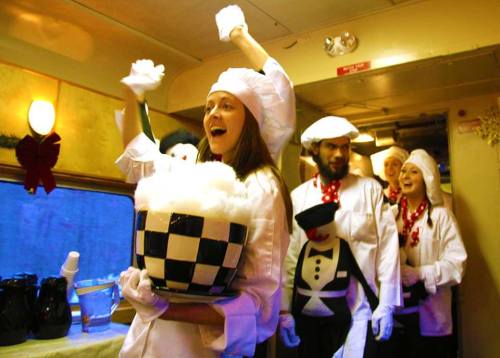 A group of people in chef outfits celebrating on a train, holding a large bowl and smiling joyfully.