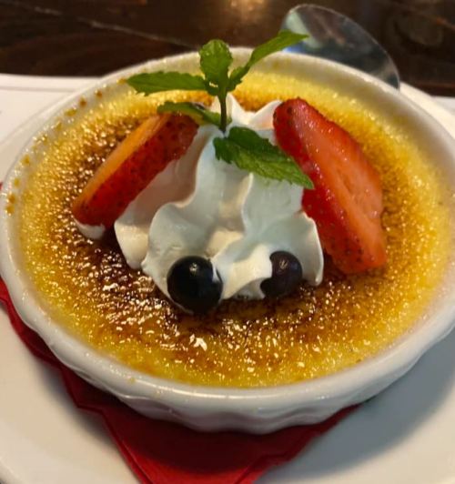 A creamy dessert topped with whipped cream, strawberries, and blueberries, served in a ramekin with a caramelized crust.