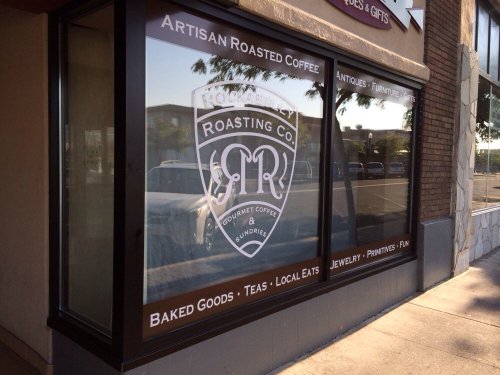 Window display featuring "Roasting Co." logo, promoting artisan coffee, baked goods, teas, and local gifts.
