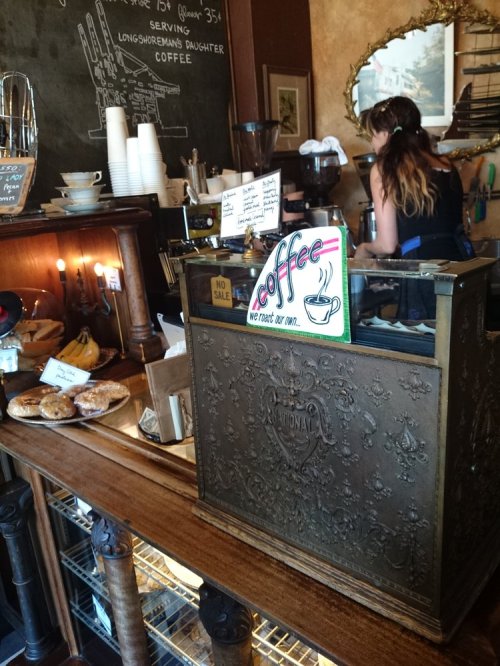 A cozy coffee shop counter with pastries, a vintage cash register, and a barista preparing drinks in the background.