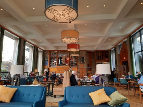 A cozy restaurant interior with modern decor, large windows, and patrons enjoying their meals at various tables.
