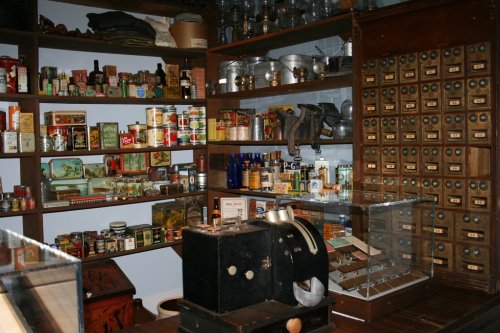 A vintage store display featuring shelves of old cans, jars, and a wooden cabinet with labeled drawers.