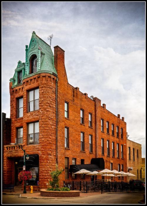 Historic red brick building with a green copper roof and outdoor seating area, set against a cloudy sky.