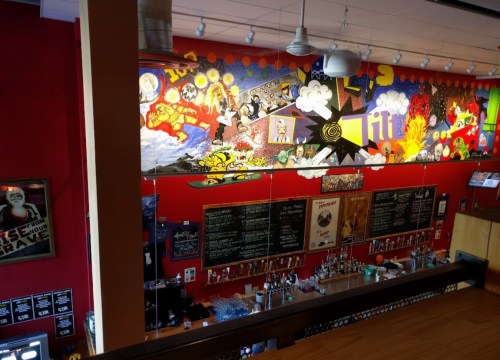 A vibrant bar interior featuring a colorful mural and chalkboard menus against red walls.