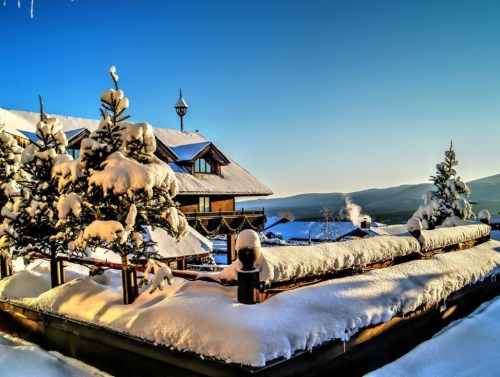 A snowy landscape featuring a cozy lodge and snow-covered trees under a clear blue sky.