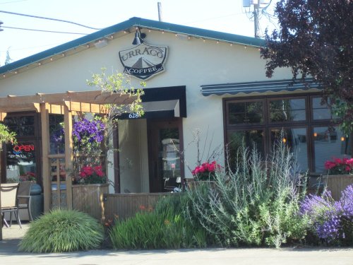 A cozy coffee shop with a sign, outdoor seating, and colorful flowers in front.