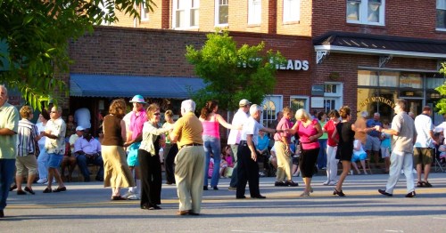 A lively street scene showcasing a community dance event in Charleston, SC, surrounded by spectators and local businesses.