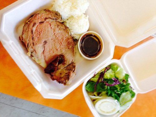 A takeout container with sliced prime rib, rice, a small cup of sauce, and a side salad with dressing.