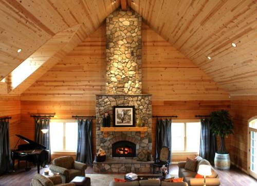 Cozy living room with a stone fireplace, wooden walls, a grand piano, and comfortable seating. Warm and inviting atmosphere.