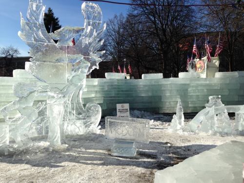A winter scene featuring intricate ice sculptures and a frosty backdrop with flags and trees.