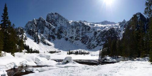 A panoramic view of snow-covered mountains and a frozen landscape under a clear blue sky. Sunlight shines brightly.