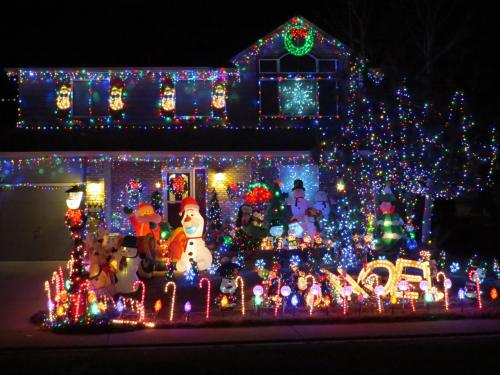 A brightly lit house decorated for the holidays with colorful lights, inflatable snowmen, and festive ornaments.