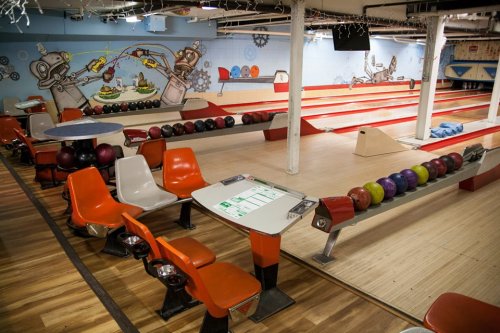 A vibrant bowling alley with colorful lanes, seating, and a playful mural on the wall.