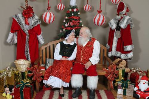 A cheerful Santa and Mrs. Claus sit together on a bench, surrounded by Christmas decorations and gifts.