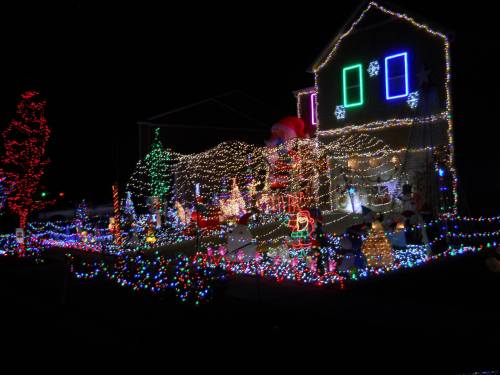 A house decorated with colorful Christmas lights, featuring festive figures and a large Santa Claus.