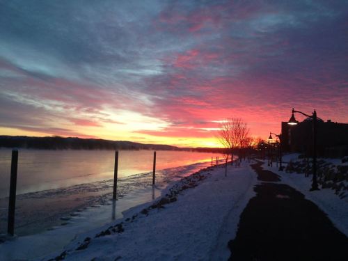 A serene winter sunset over a frozen river, with colorful skies and snow-covered banks lining the path.