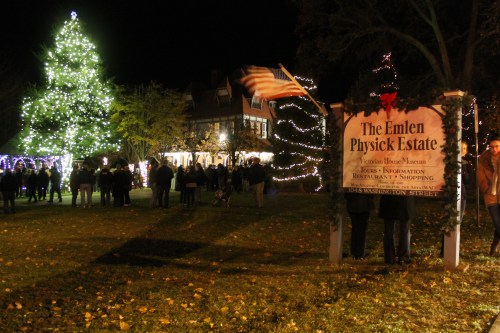A festive night scene at the Emlen Physick Estate, featuring a lit Christmas tree and holiday decorations.