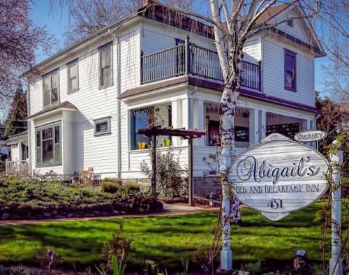 A charming white bed and breakfast with a sign, surrounded by greenery and a well-maintained garden.