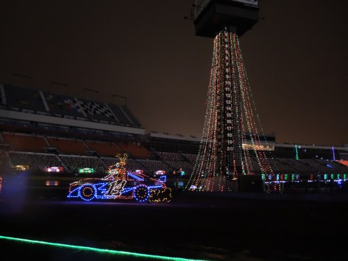 A brightly lit race car decorated with colorful lights, set against a dark stadium backdrop.