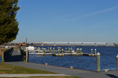 A serene waterfront scene featuring a dock, a boat, and a bridge in the background under a clear blue sky.