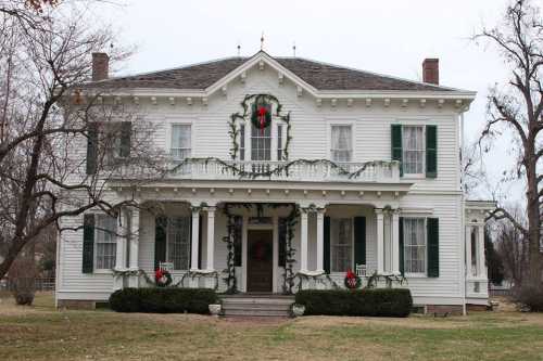 A white, two-story house decorated with greenery and red wreaths for the holidays, surrounded by bare trees.