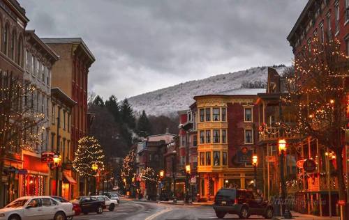 A charming street lined with festive lights and snow-capped mountains in the background under a cloudy sky.