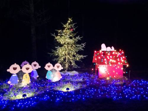 Colorful holiday display featuring a decorated tree, a lit house, and cheerful cutouts of children.