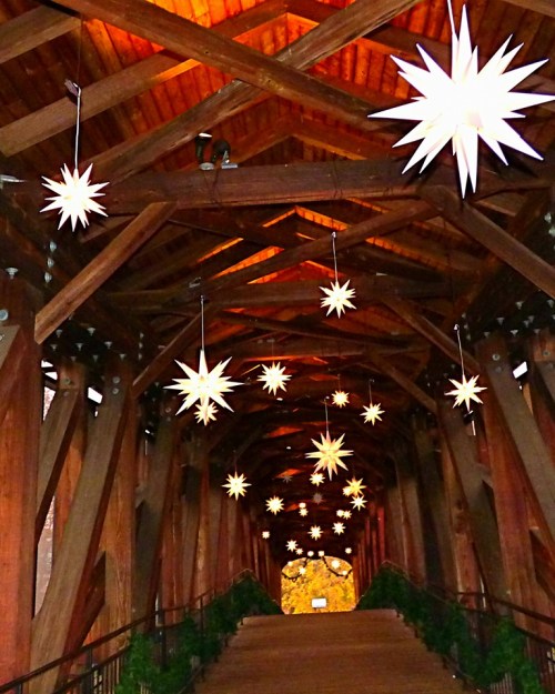 A wooden bridge adorned with hanging star-shaped lights, creating a warm, inviting atmosphere.